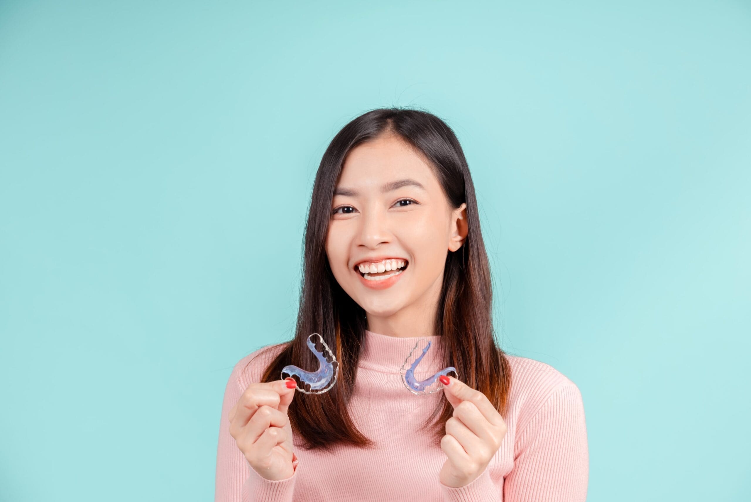 Girl holding retainers Clear aligners and Hawley retainer for post-treatment orthodontic care.