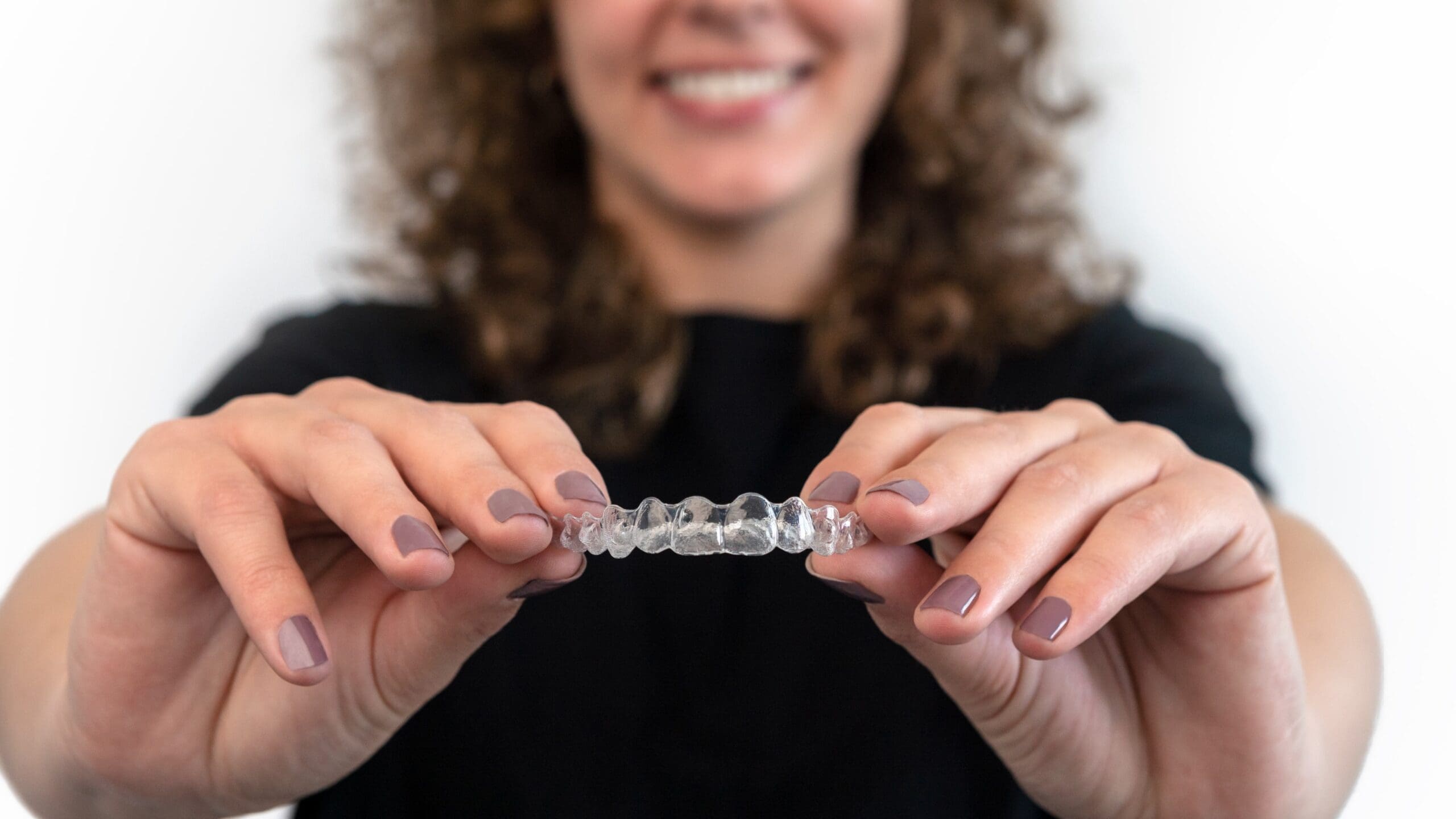 Girl smiling brightly while holding retainers Happy girl smiling with clear retainers for a healthy smile