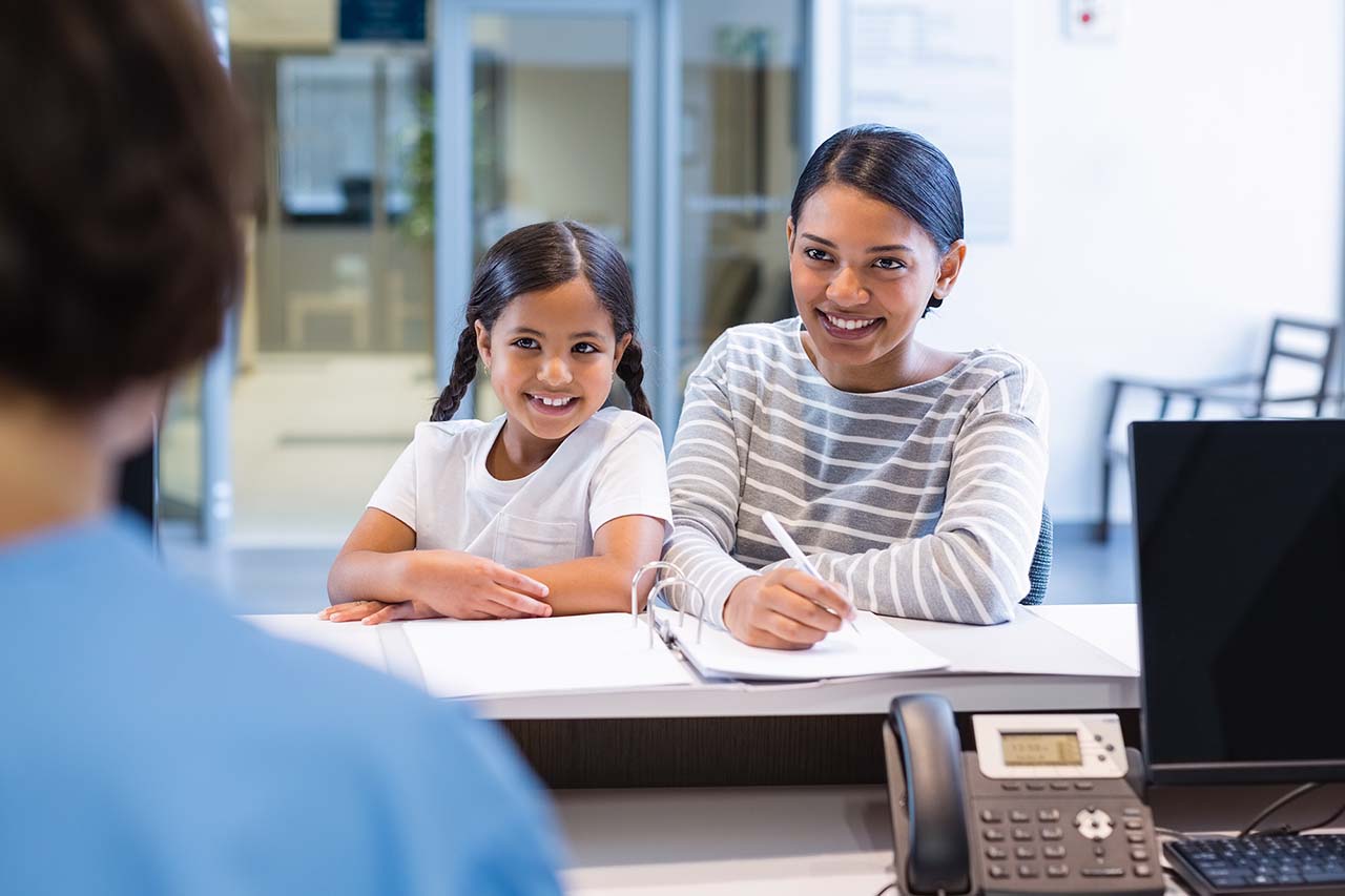 mother with her daughter filling out paperwork at front desk Mother and daughter discussing orthodontic treatment plans at a dentist's office. Patient consultation, braces, dental care.