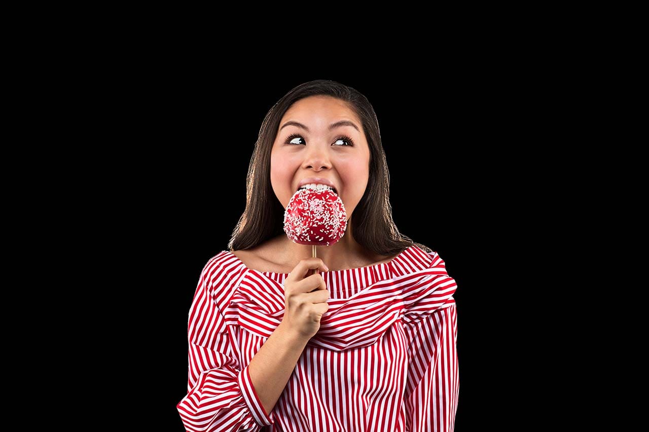 teenage girl enjoys a candied apple Teenage girl smiling and enjoying a candied apple, showcasing healthy teeth and a confident smile after Invisalign treatment.