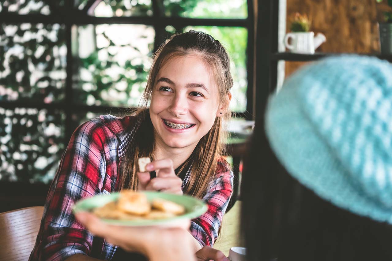 teenage girl in braces eating a snack at home Teenage girl smiling with braces while eating a healthy snack at home.
