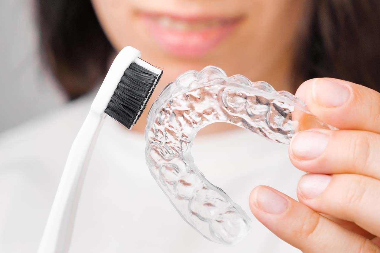 woman cleaning her clear aligner with a toothbrush Woman brushing clear aligner with toothbrush, dental hygiene for braces, orthodontic care
