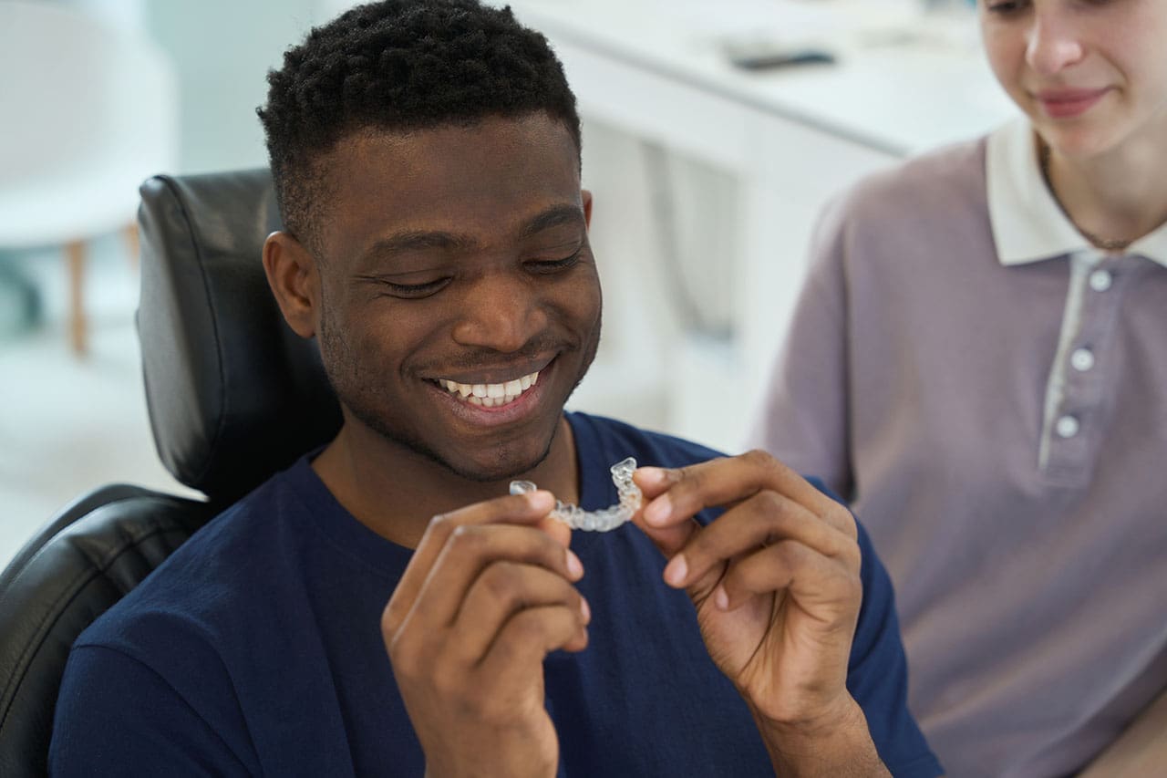 young man checking out his new clear orthodontic aligner Man holding and examining transparent orthodontic aligners. Effective teeth straightening with Sure smile.