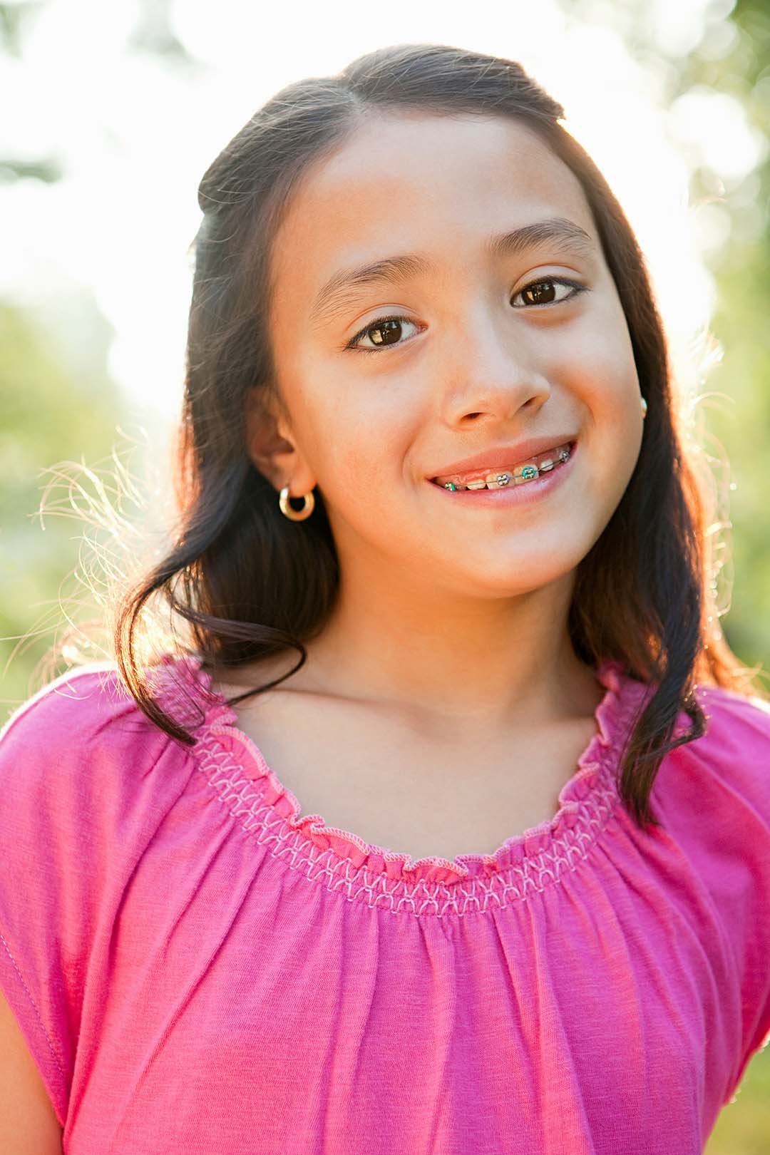 Girl with multicolored braces smiling for a portrait outside Ferri Orthodontics treats all ages, including children