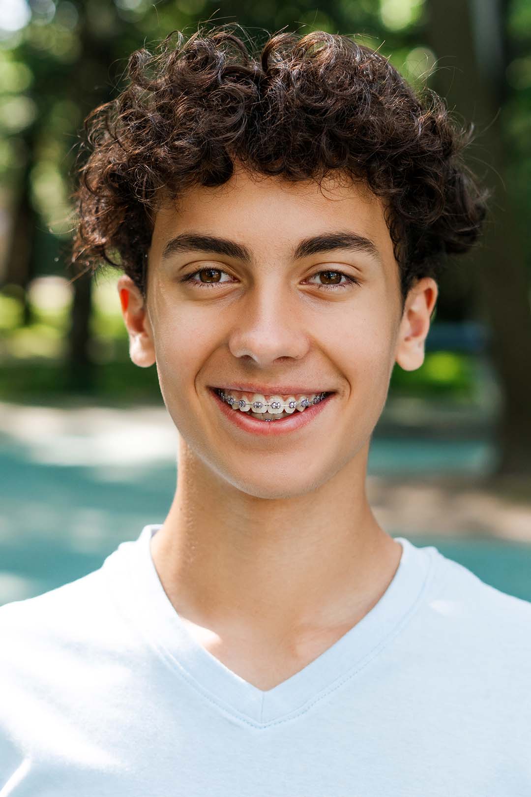 happy teenage boy with braces smiles outside Ferri Orthodontics treats people of all ages, including teens